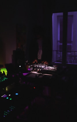 A moody, dark-themed DJ studio with turntables and sound equipment glowing under soft blue lights.