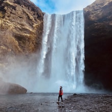 man in red jacket standing near waterfalls during daytime