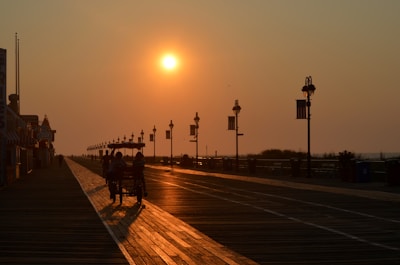 Sunset casting warm golden light over the palm-lined boardwalk with tourists strolling and enjoying the view.