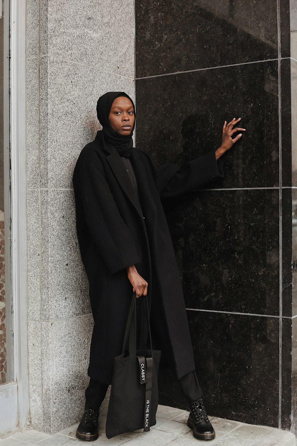 Mujer con hiyab negro de pie junto a la pared negra