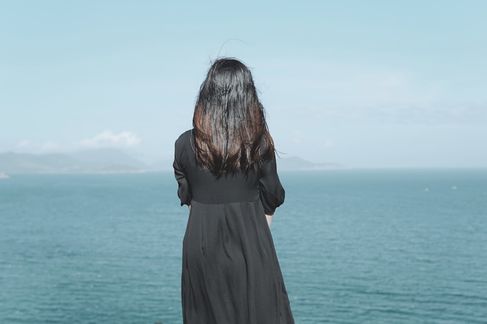 woman in black dress standing by the sea during daytime
