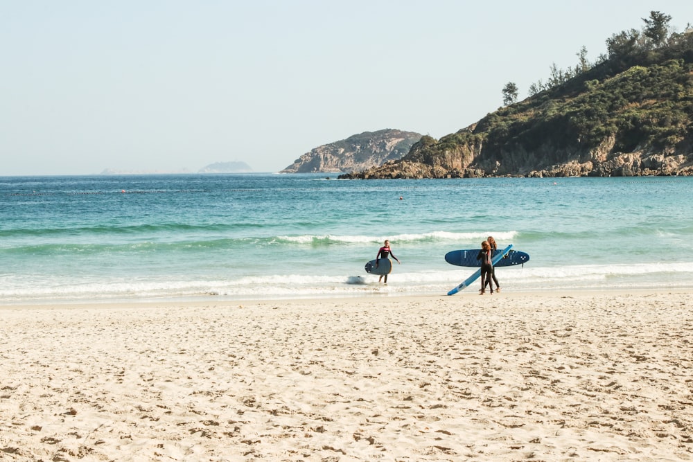 man in blue shirt carrying blue surfboard on beach during daytime