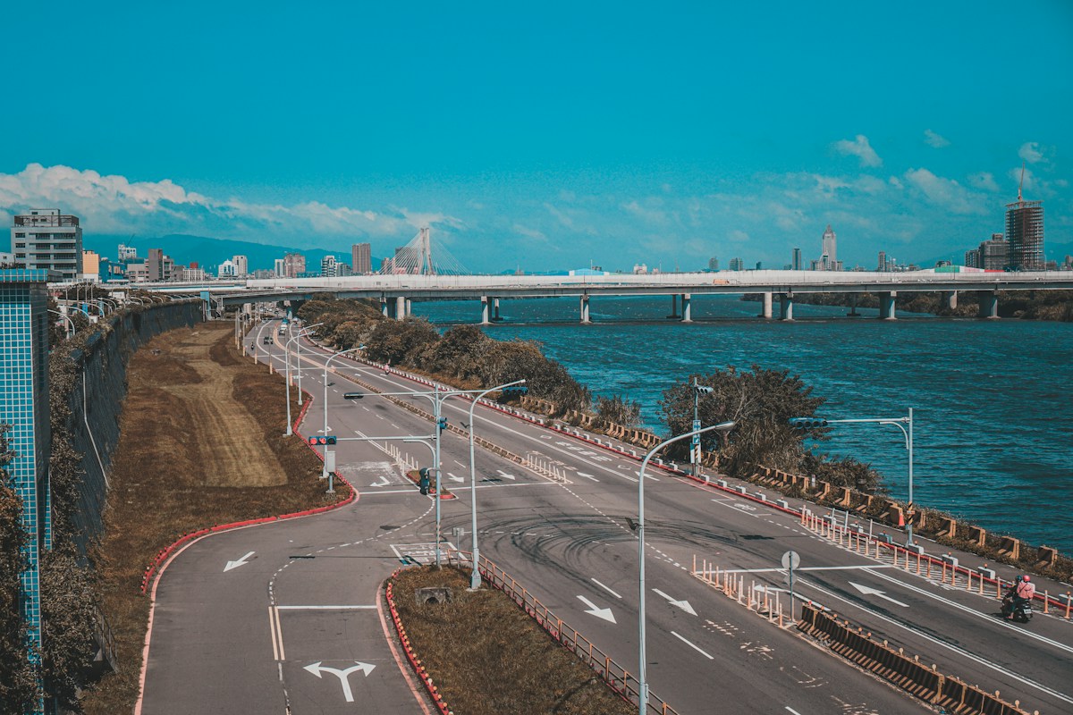 A multi-lane riverside road with painted turn arrows and a bridge over the river in New Taipei, Taiwan