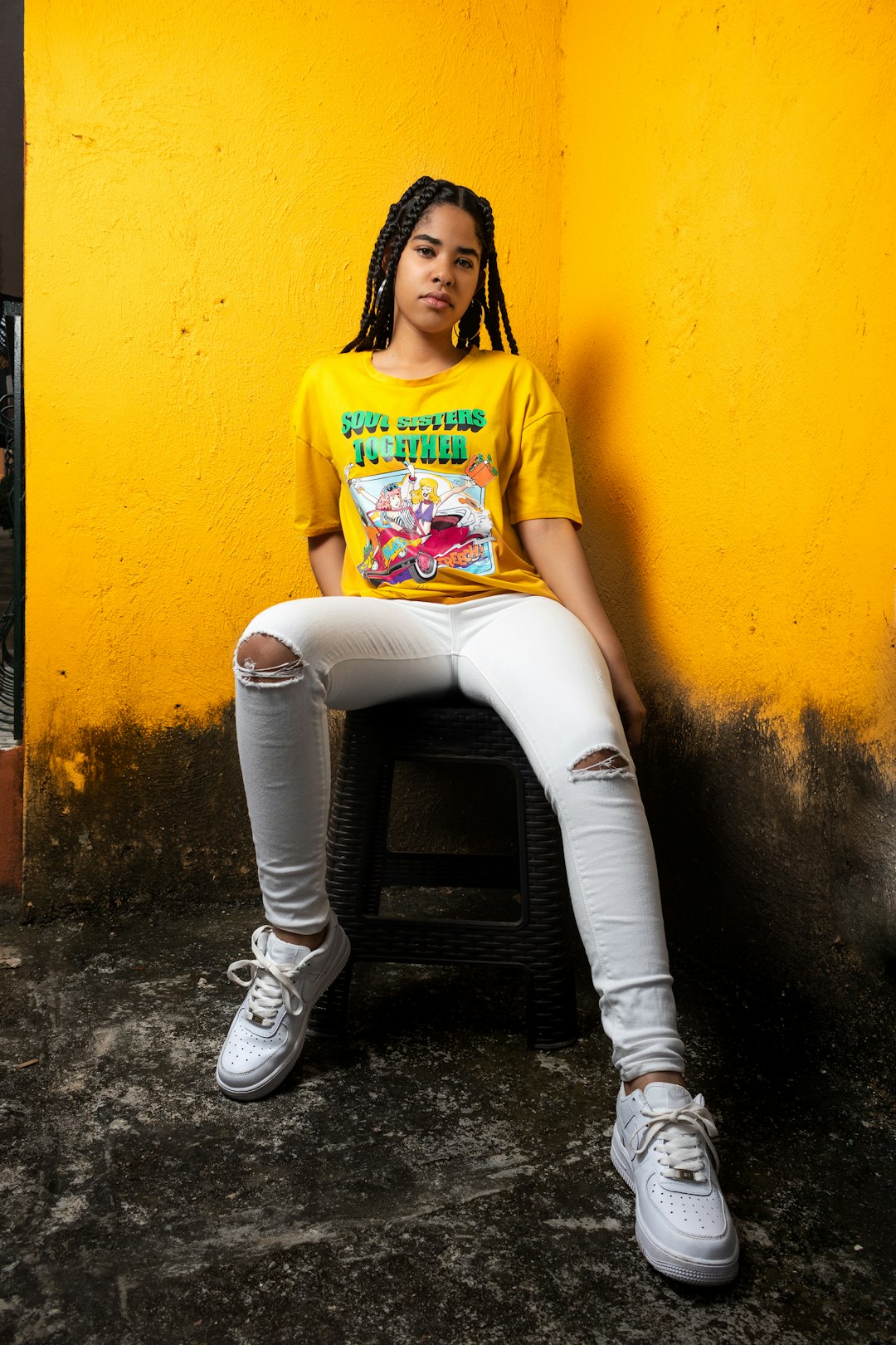 woman in yellow crew neck t-shirt and white pants sitting on black concrete floor