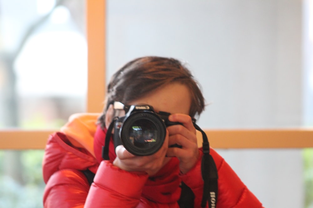 man in red jacket holding black dslr camera