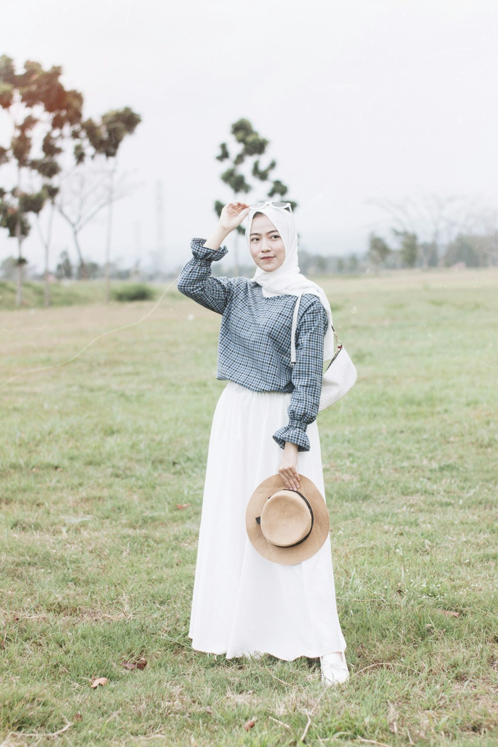 woman in white long sleeve dress holding brown hat standing on green grass field during daytime