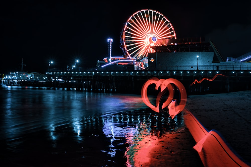 red and white ferris wheel near body of water during night time