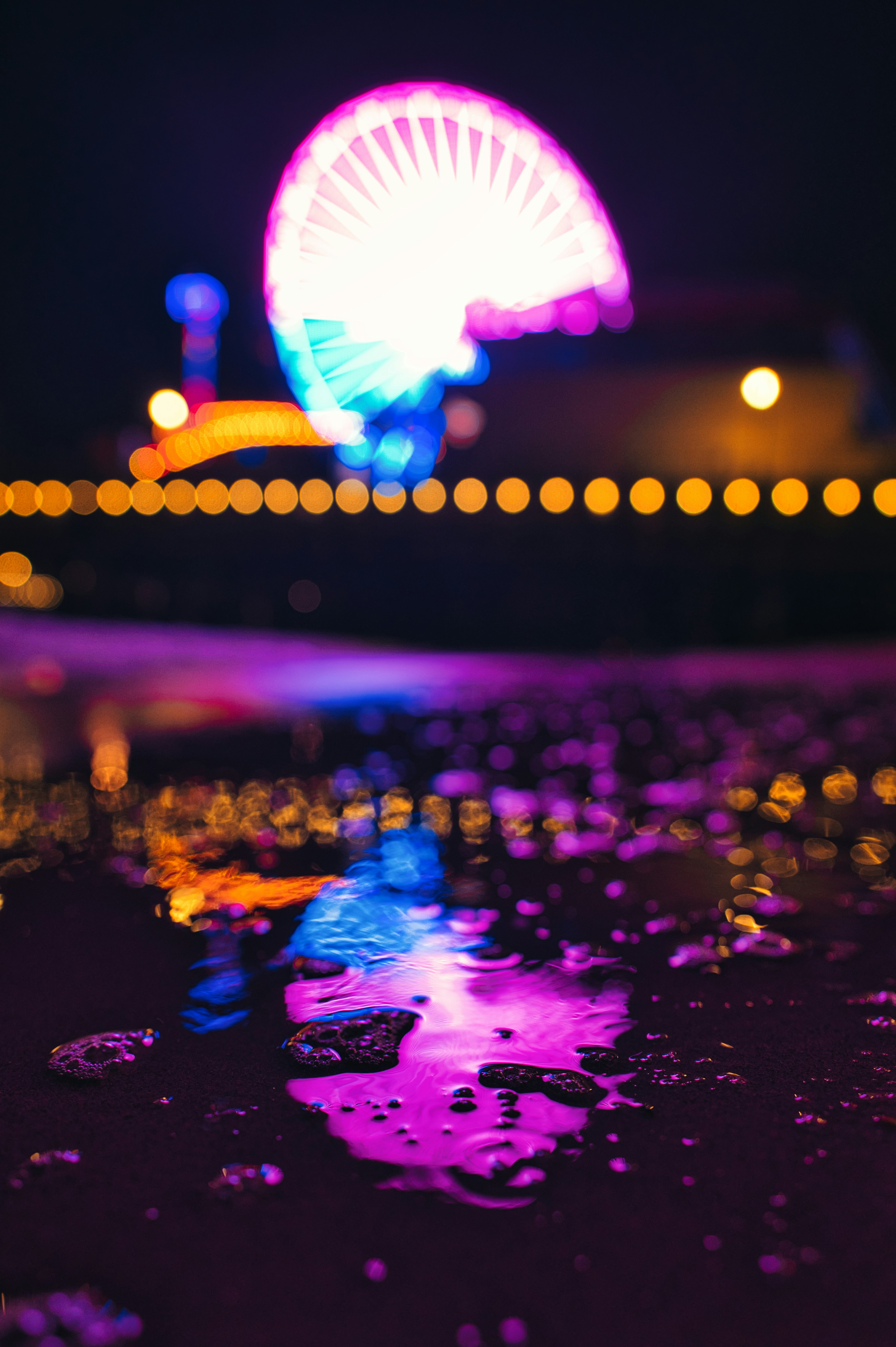 Ferris wheel at night reflected in ocean on the beach. 