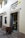 A brown alpaca stands on a cobblestone street, peering into a bakery shop. The shop, named 'El Buen Pastor', has its name and details written on the wall beside the door. The bakery's display case is visible through the open door, filled with pastries.