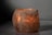 A glowing Himalayan salt lamp with a rough, textured surface emits a warm, amber light. The lamp sits on a smooth, neutral-colored surface against a plain background, creating a calming and serene atmosphere.