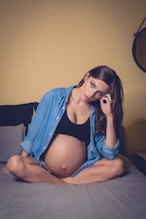 woman in blue denim jacket and black brassiere sitting on bed