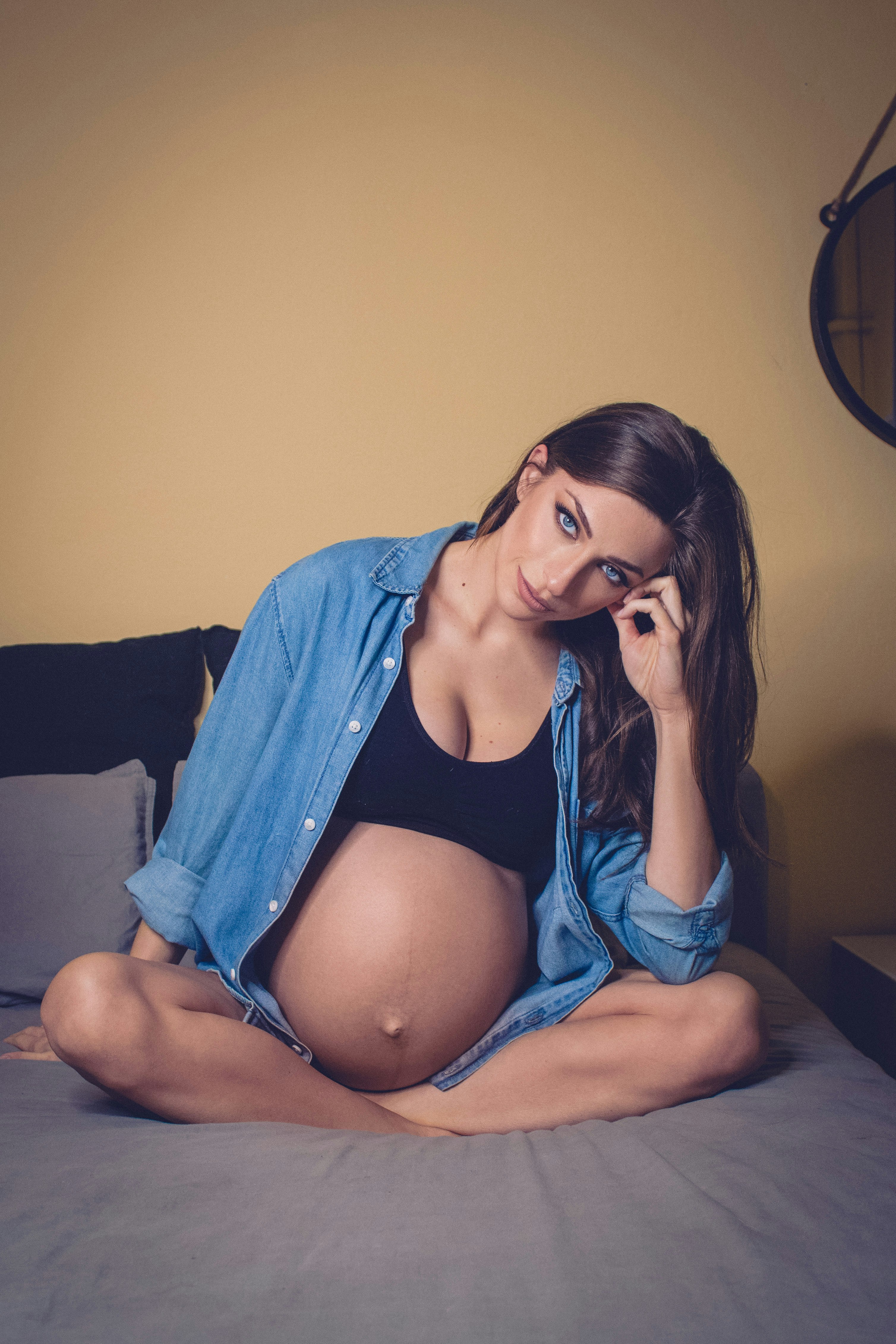 woman in blue denim jacket and black brassiere sitting on bed