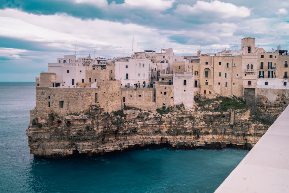 white concrete building on brown rock formation beside blue sea under white clouds and blue sky