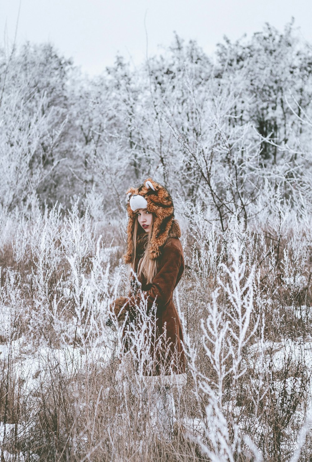 woman in brown coat standing on white grass field during daytime