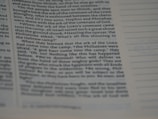 A close-up view of a page from a book with text printed in columns. The focus is on the left side, where the text is clear and contains sections of dialogue and narrative. The right side of the page is out of focus, showing dotted lines possibly meant for notes or annotations.