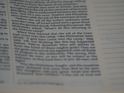 A close-up view of a page from a book with text printed in columns. The focus is on the left side, where the text is clear and contains sections of dialogue and narrative. The right side of the page is out of focus, showing dotted lines possibly meant for notes or annotations.