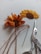 Two pieces of embroidery resembling sunflowers are displayed on a light background. One is partially completed with orange and yellow threads still attached. Beside it, there is a pair of ornate scissors and a needle.