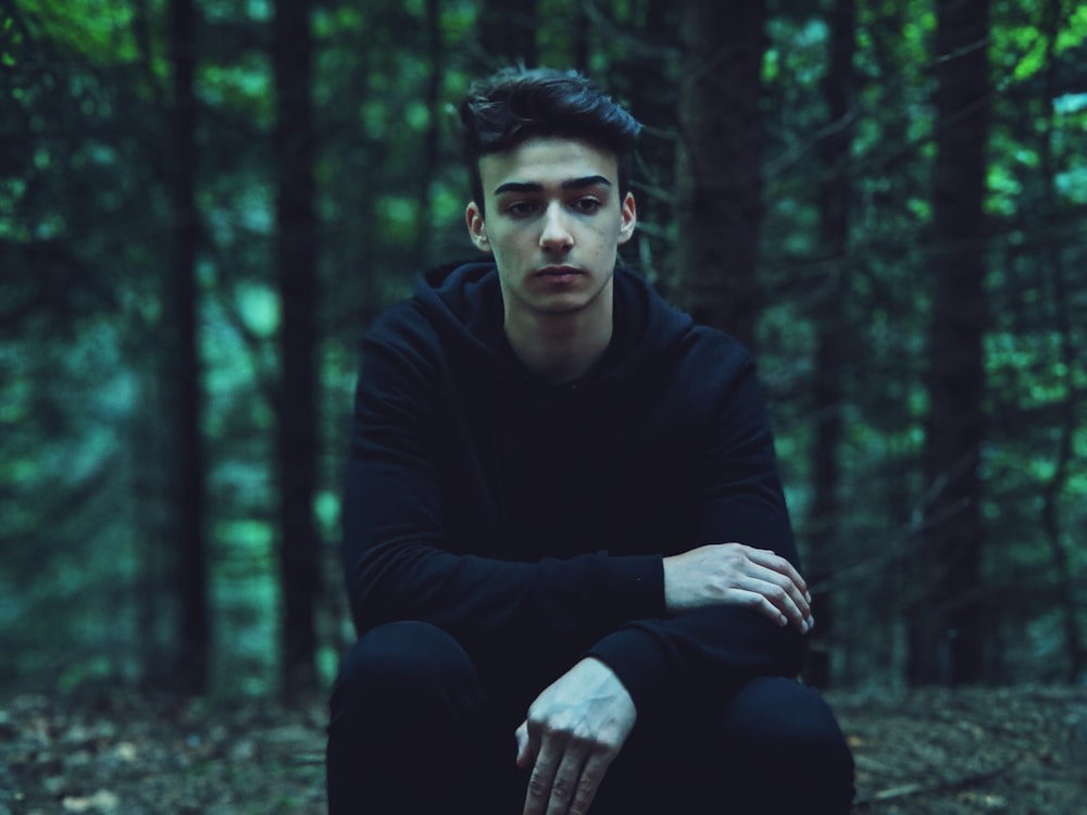 man in black long sleeve shirt sitting on ground surrounded by trees