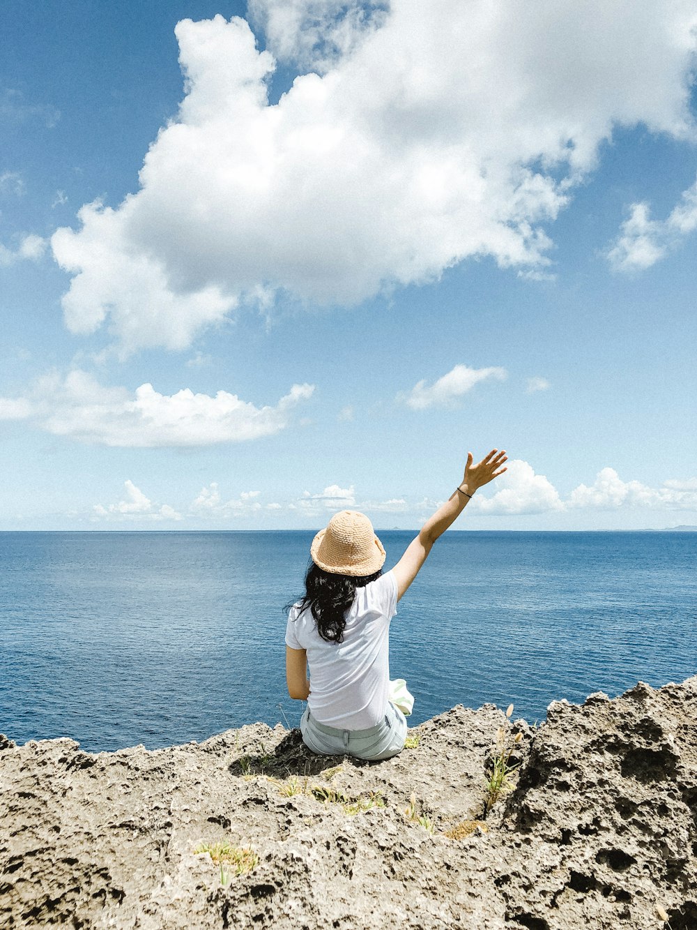 woman in white shirt and black pants sitting on rock near sea during daytime