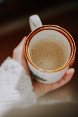 A cozy kitchen scene with a hand holding a softly textured ceramic mug filled with steaming coffee.
