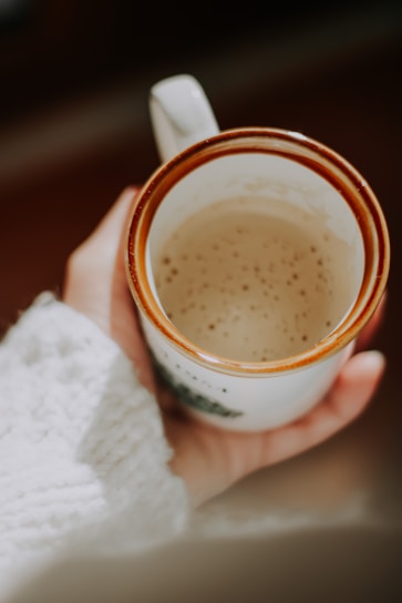 A cozy kitchen scene with a hand holding a softly textured ceramic mug filled with steaming coffee.