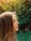 Portrait of a thoughtful woman standing in a lush forest with sunlight filtering through the leaves.
