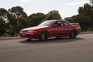 A shiny red sports car speeding along a coastal highway, with motion blur capturing its speed.