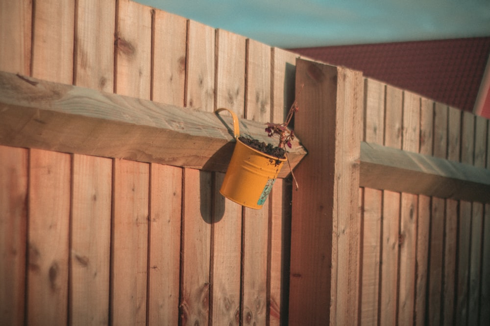 orange and brown watering can hanged on brown wooden fence