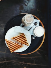 A colorful plate featuring a toasted panini, fresh sandwich, and a tall creamy milkshake.