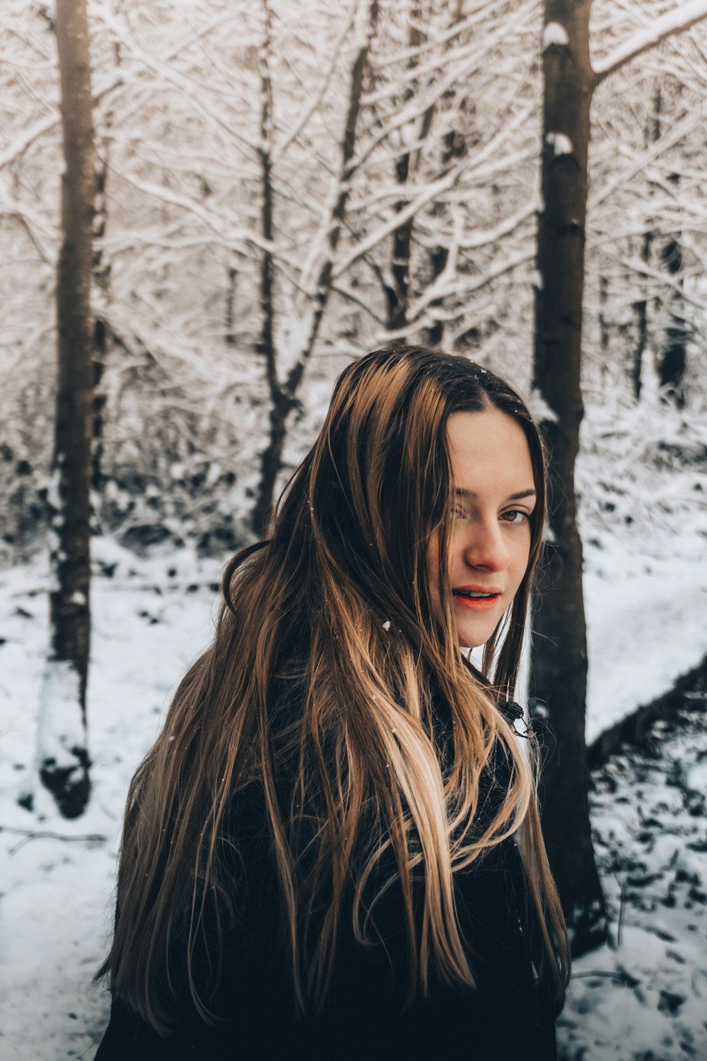 woman in black jacket standing near brown bare trees during daytime