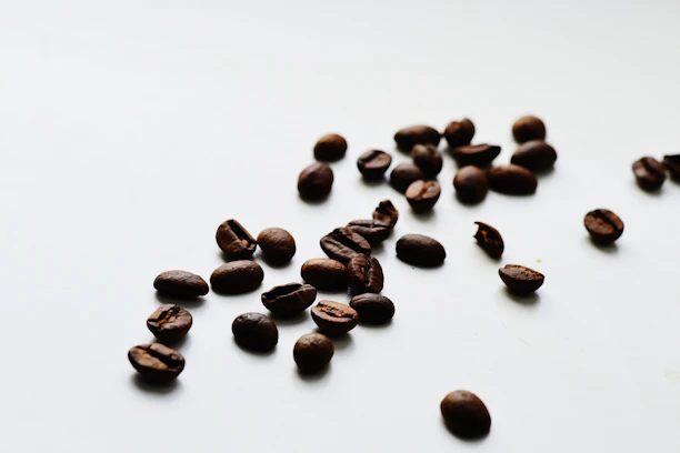 Minimalist shot of premium coffee beans scattered on a white surface with soft shadows.