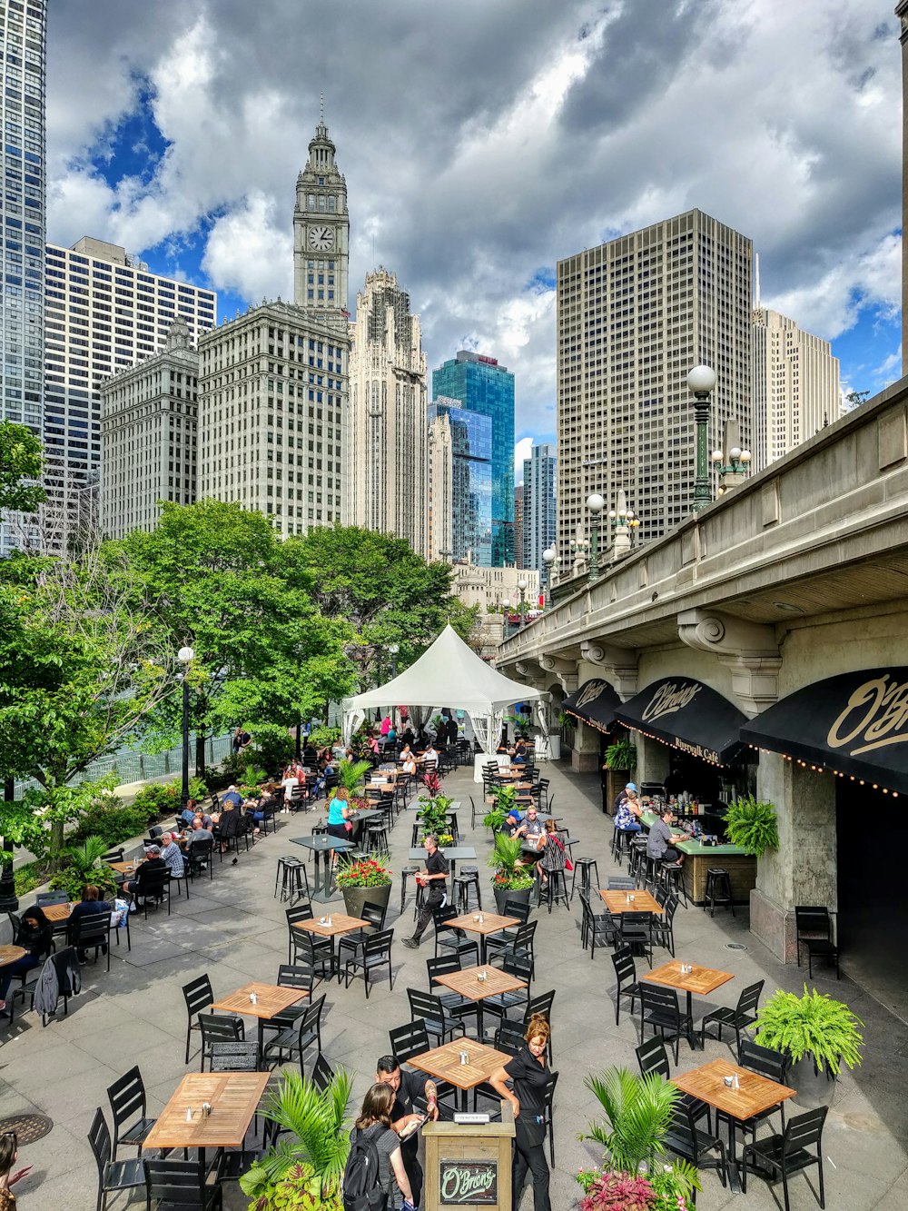 people sitting on chairs near green trees and buildings during daytime