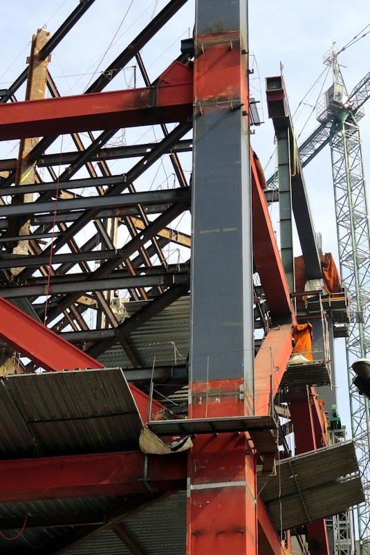A construction site showing steel structural frames under assembly with cranes in the background.