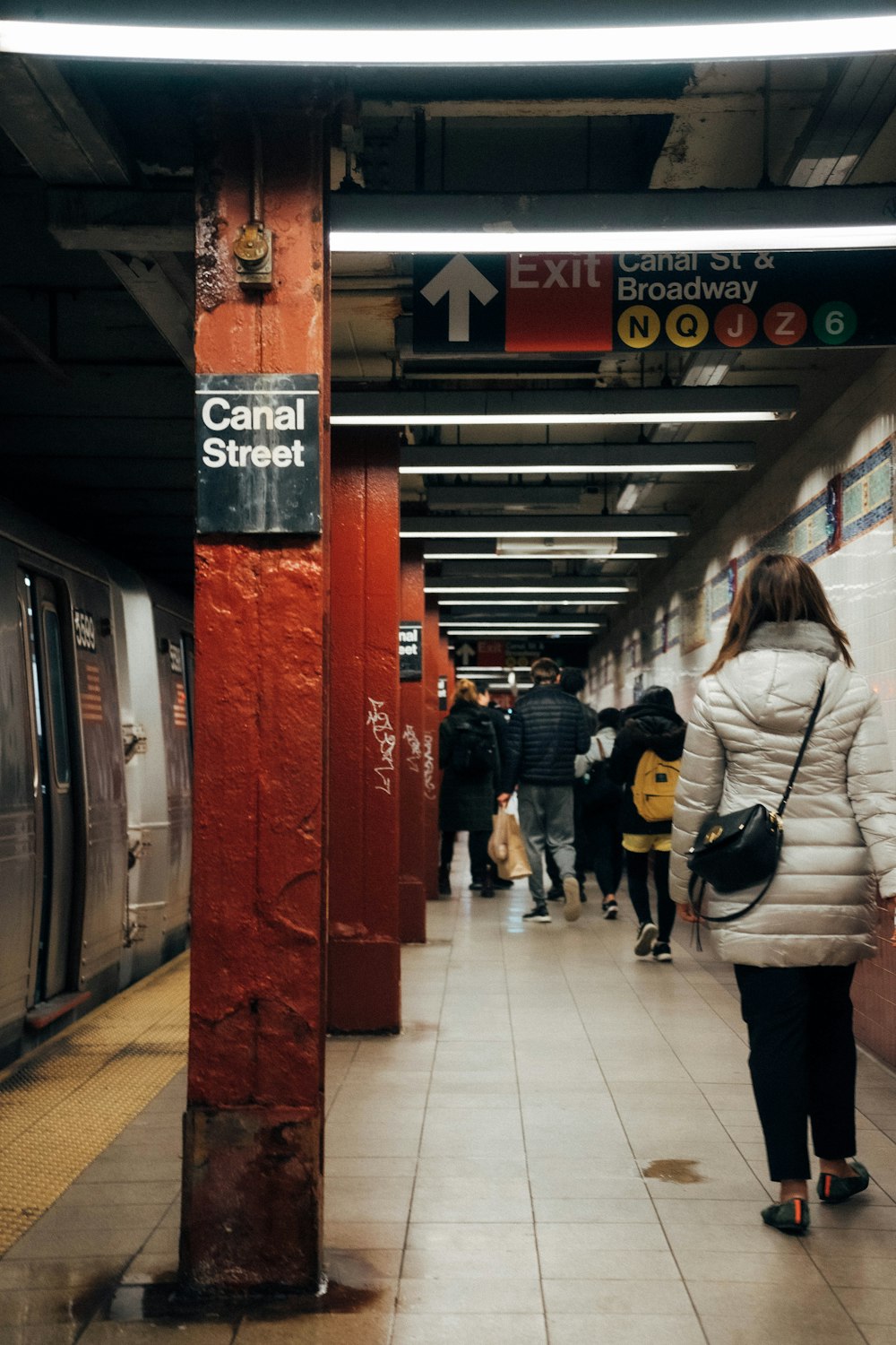 woman in white jacket and black pants carrying black backpack walking on sidewalk