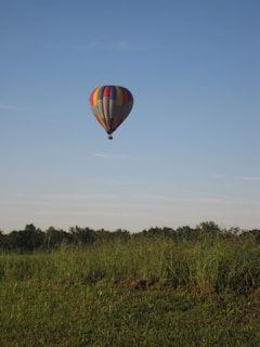 A happy couple smiling inside the basket of a hot air balloon floating peacefully above lush green fields.