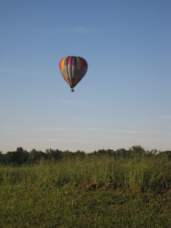 A happy couple smiling inside the basket of a hot air balloon floating peacefully above lush green fields.