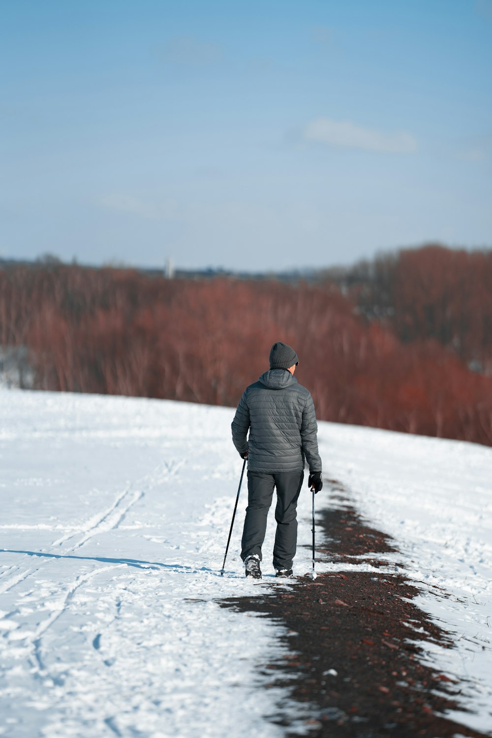 灰色のジャケットと黒いズボンを着た男性が昼間、雪に覆われた地面を歩く