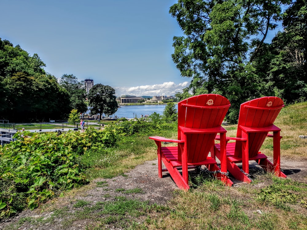 red wooden armchairs on green grass field near body of water during daytime