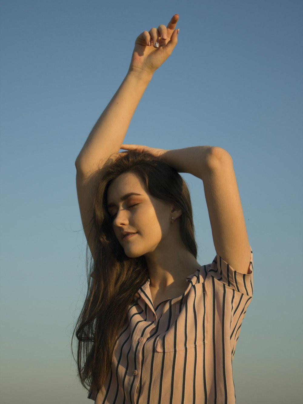 woman in white and black stripe button up shirt raising her right hand