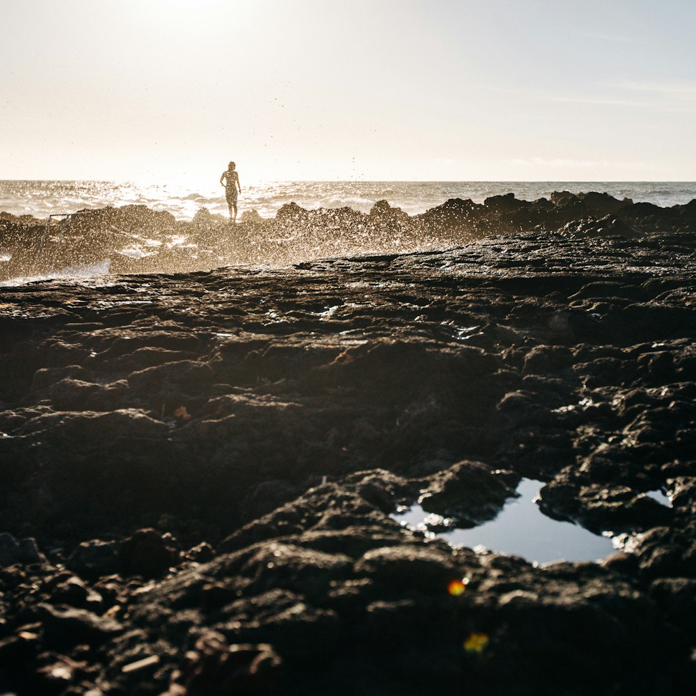 Persona in piedi sulla formazione rocciosa di fronte all'acqua dell'oceano durante il giorno
