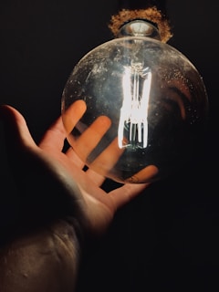 A friendly electrician smiling while holding a light bulb in a bright, modern workspace.