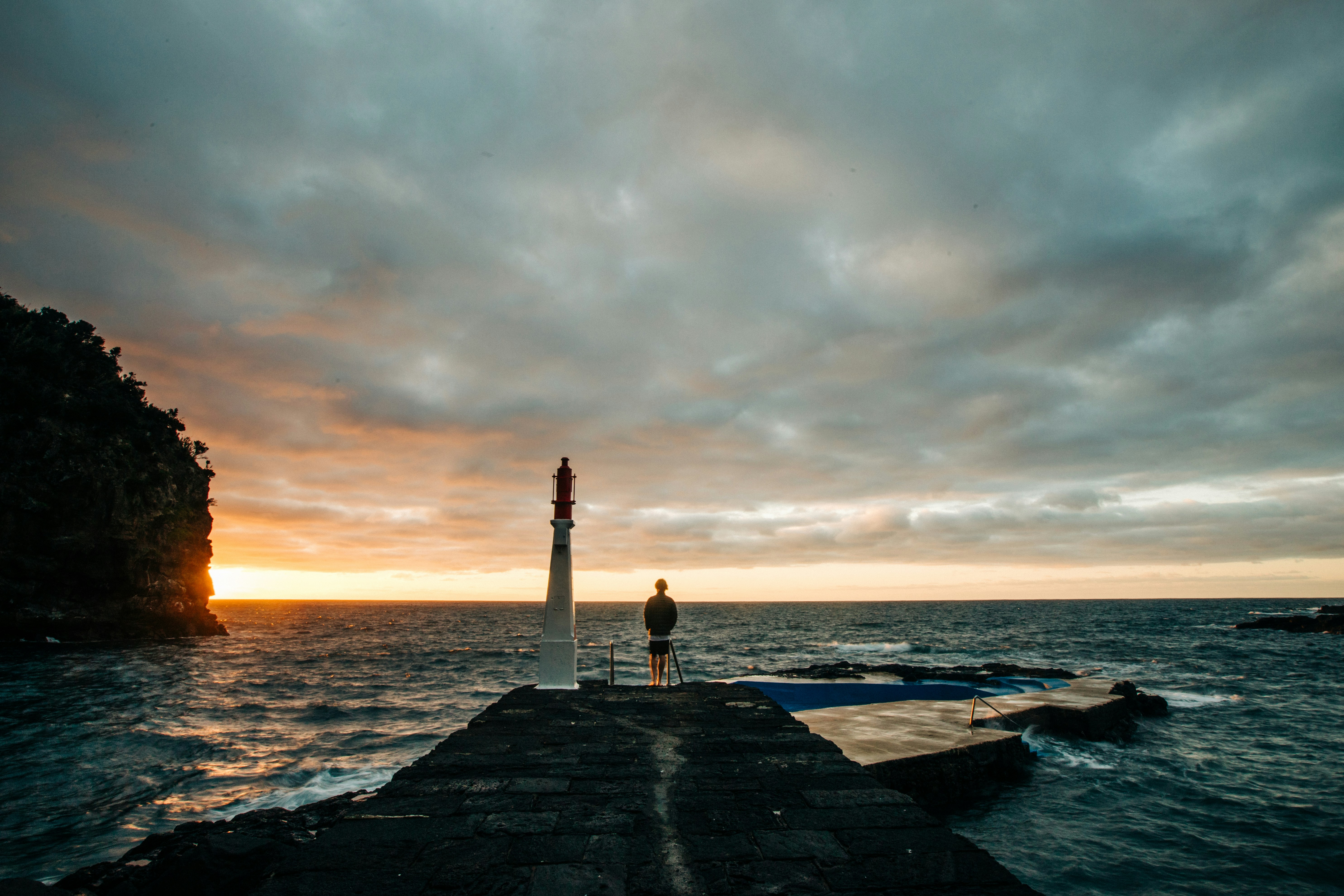 White and red lighthouse near body of water under cloudy sky during ...