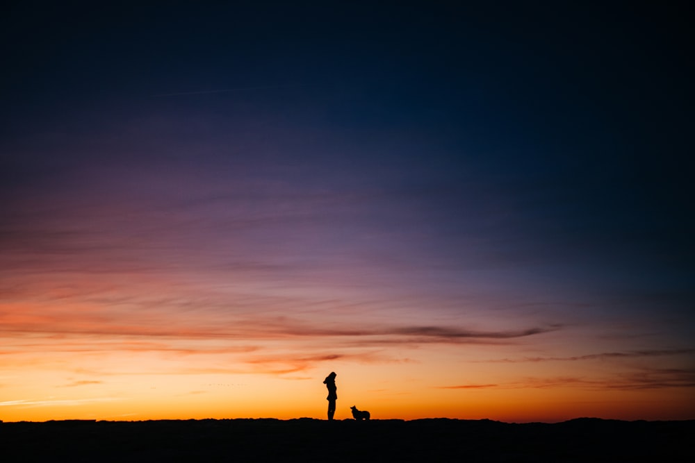 silhouette of man standing on hill during sunset