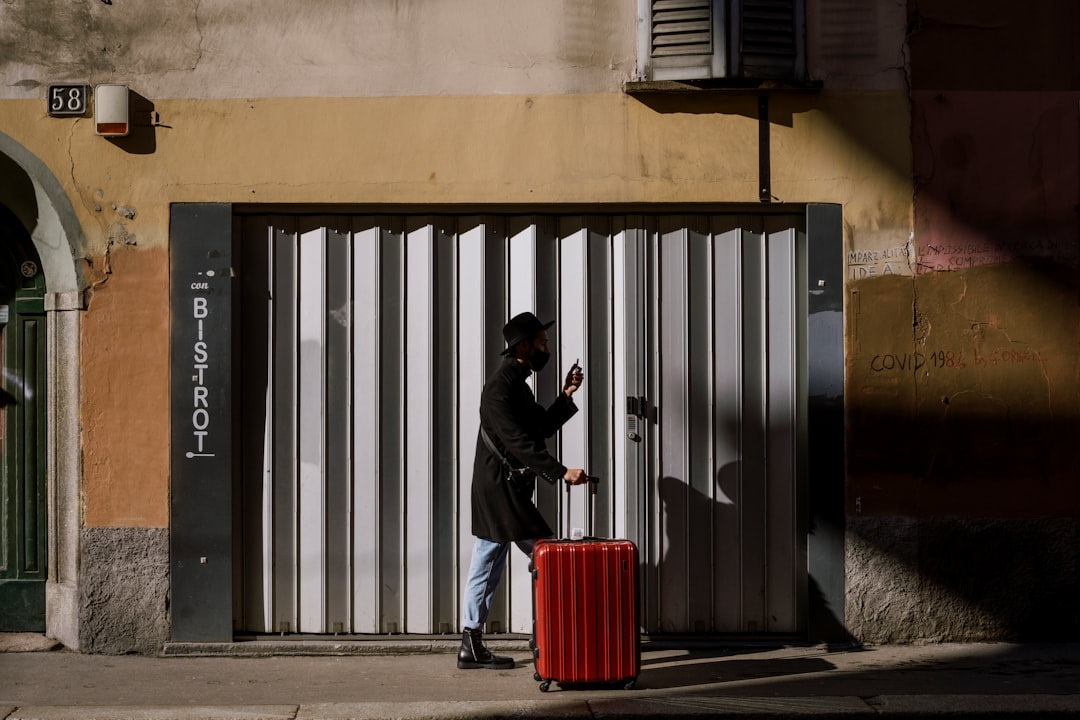 man in black jacket and blue denim jeans standing beside red trash bin