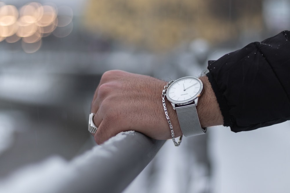 person wearing silver round analog watch with black leather strap