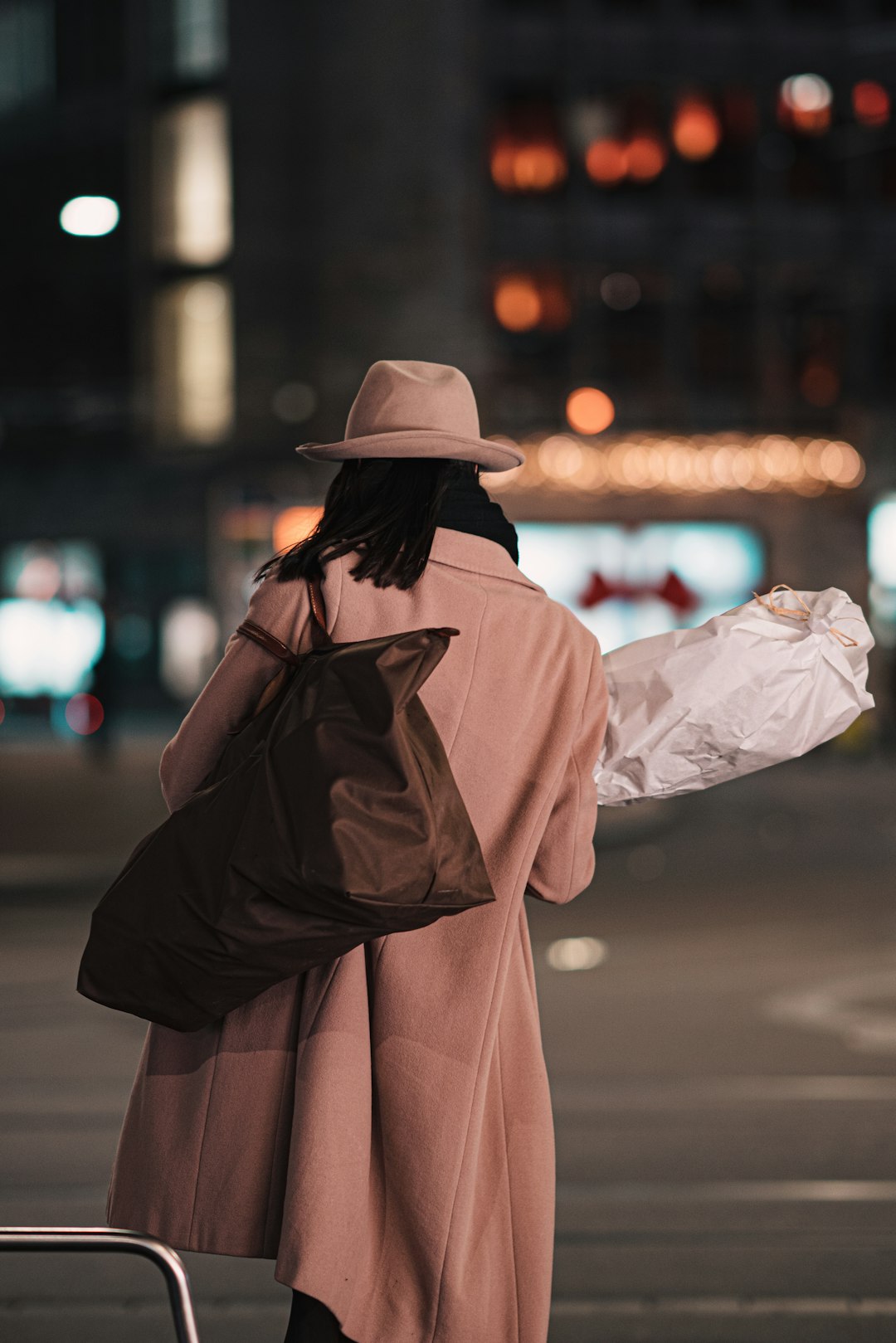 woman in brown coat and brown hat standing on sidewalk during night time