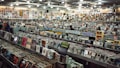 A large record store filled with rows of vinyl records and CDs. Shelves display various album covers in diverse genres, and the walls are covered with posters. Several people browse through the collection.