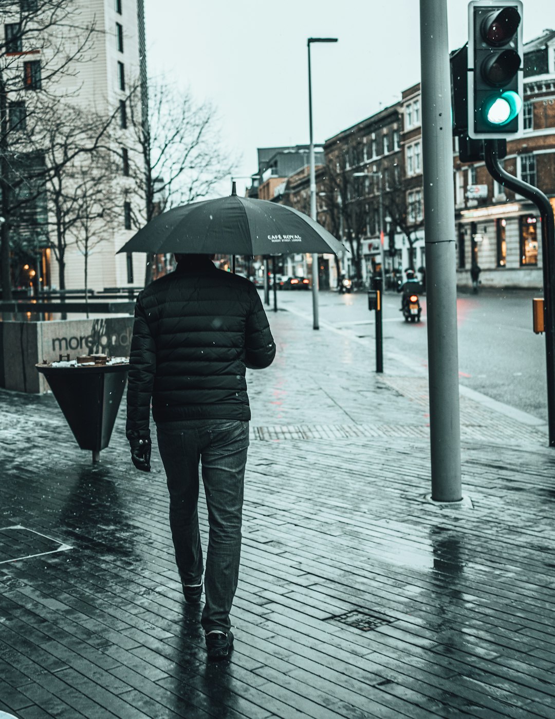 person in black jacket and blue denim jeans holding umbrella walking on sidewalk during daytime