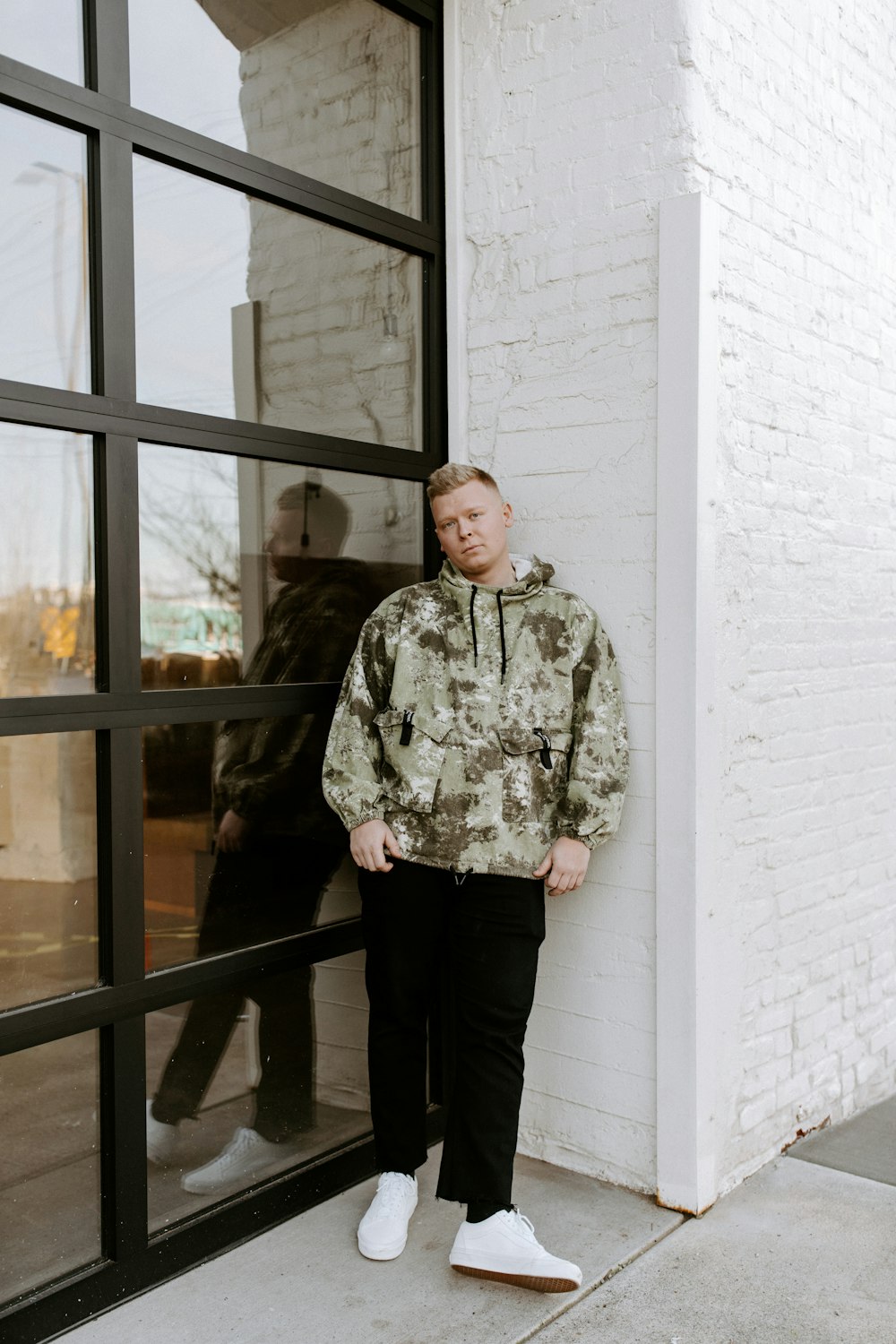 man in green and white camouflage jacket standing beside glass window