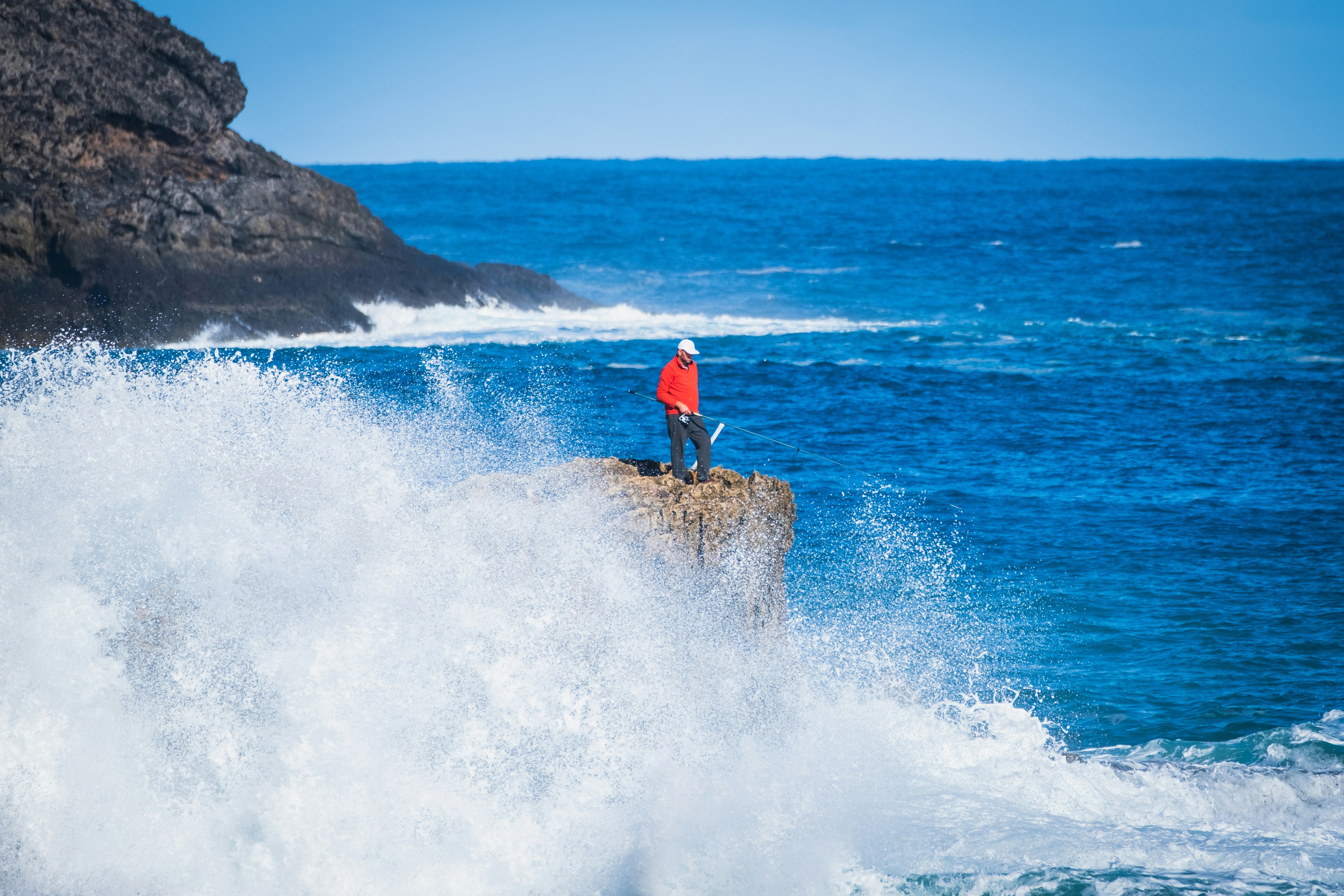 man in blue shirt and black shorts standing on rock formation near ocean waves during daytime